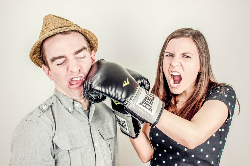 une jeune femme équipée de gants de boxe met un uppercut à un jeune homme, symbolisant un conflit au travail