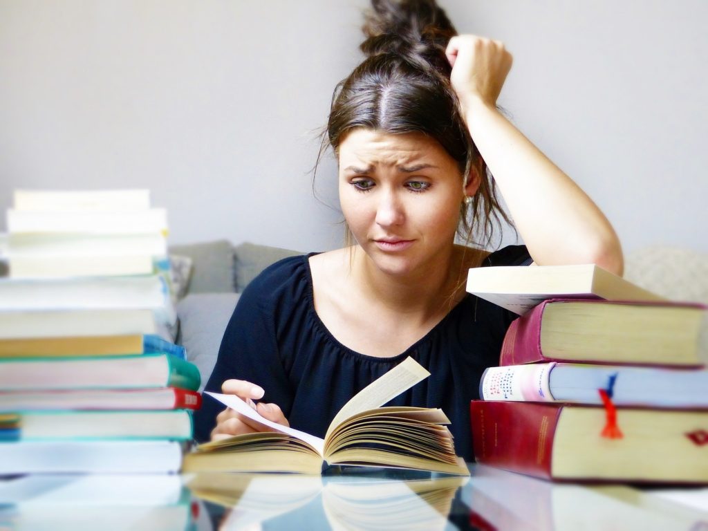 une jeune femme en stress face à des piles de livres à étudier