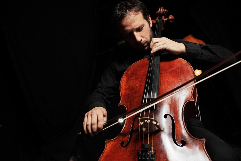 un homme glisse son archet sur les cordes d'un violoncelle, le visage concentré, il produit une musique relaxante et anti stress