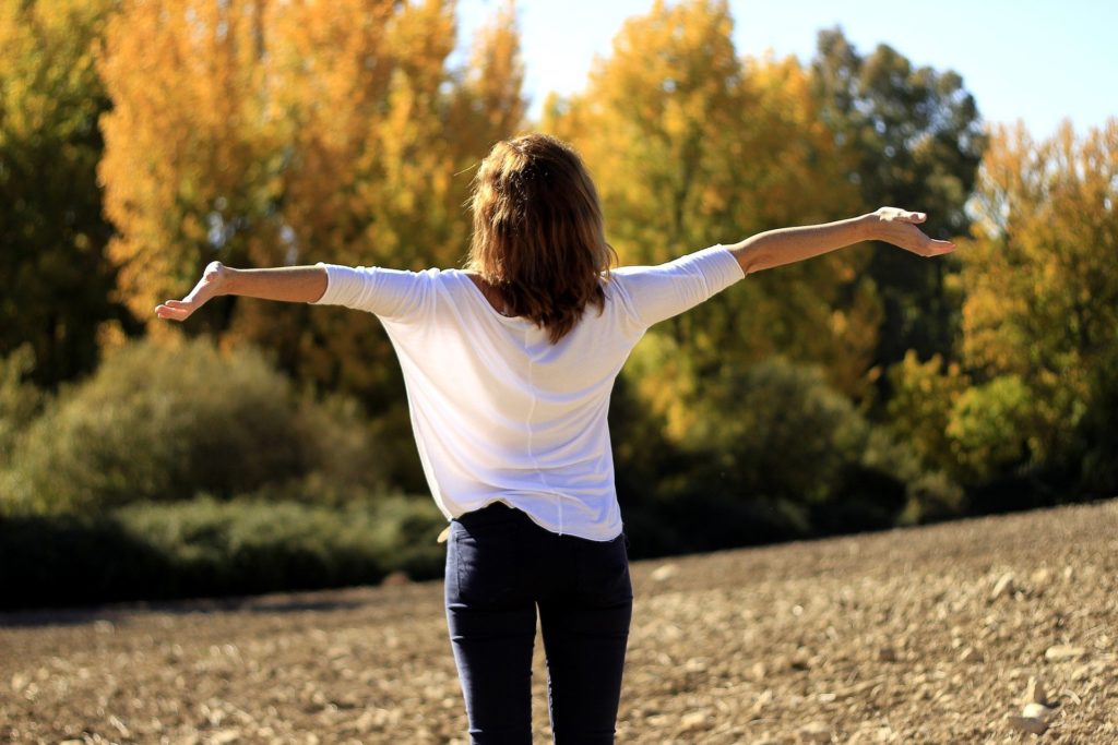 une femme de dos s'étire face à la nature, calme et sans stress