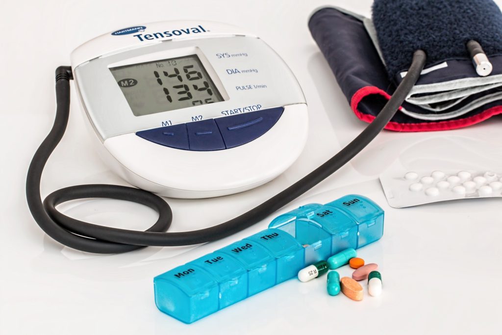 un tensiomètre électronique posé sur une table indique des chiffres trop élevés et à côté : un pilulier