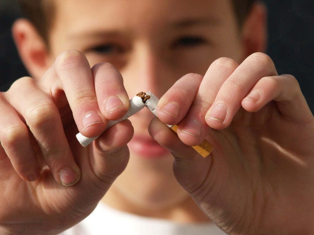 un enfant brise en 2 parties un cigarette, avec un sourire satisfait.