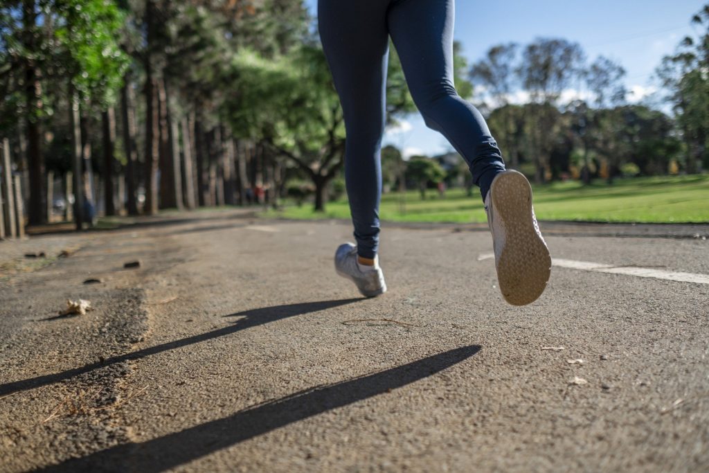 des jambes de femmes en jogging courent ente un petit bois et une pelouse